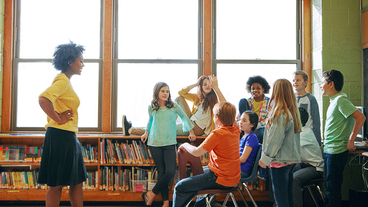 Teacher and group of students near classroom windows and a bookshelf