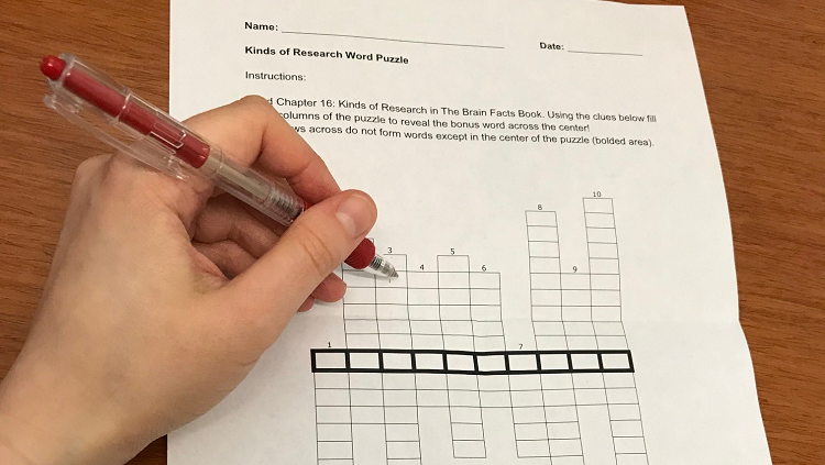Photograph of a hand writing in a crossword puzzle