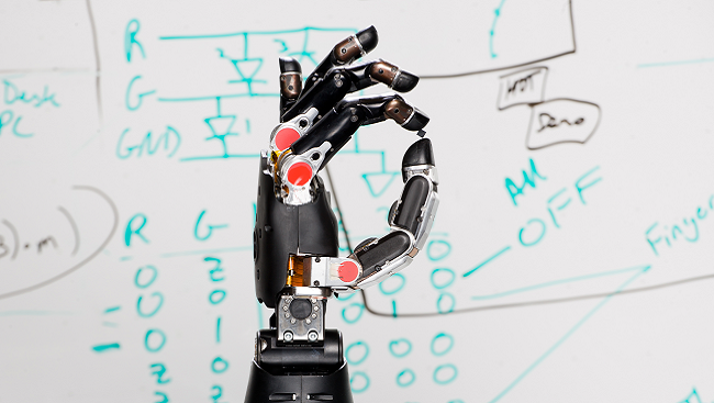 Image of a neuroprosthetic hand in front of a white marker board with calculations written on it.