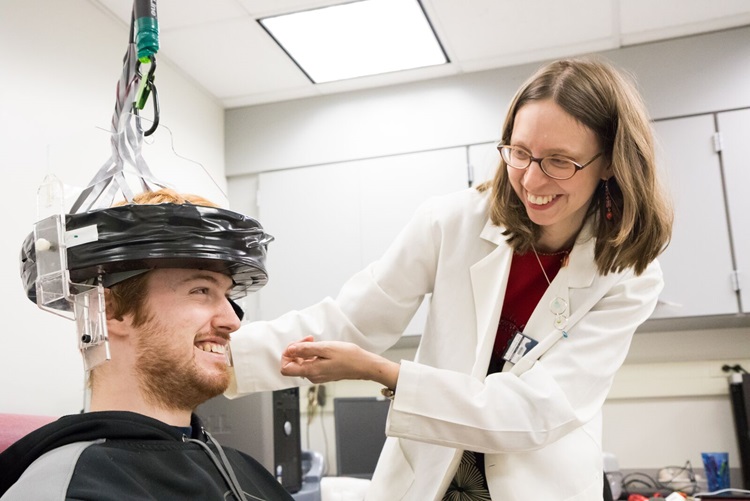 Woman smiling down at man wearing a PET scanner helmet.