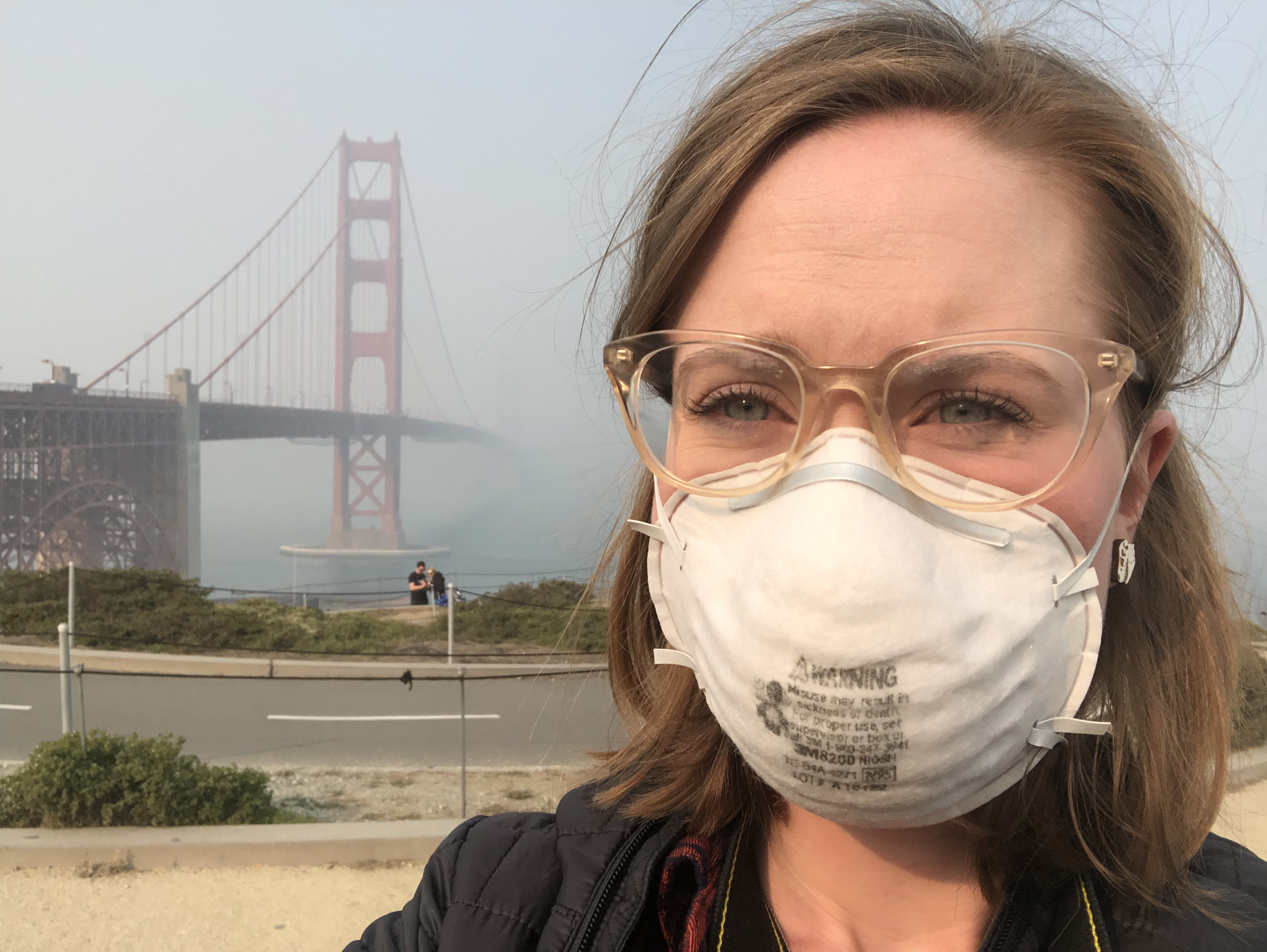 Photograph of woman with mask on in front of Golden Gate Bridge