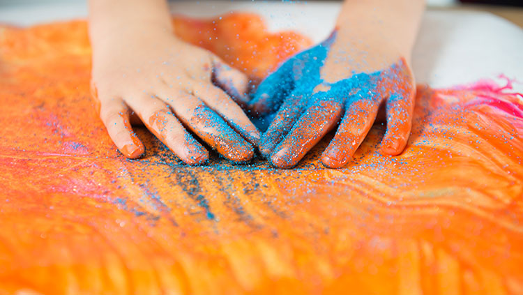 hands covered in blue glitter on orange paint
