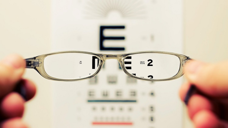 Person holding eyeglasses in front of an eye exam chart